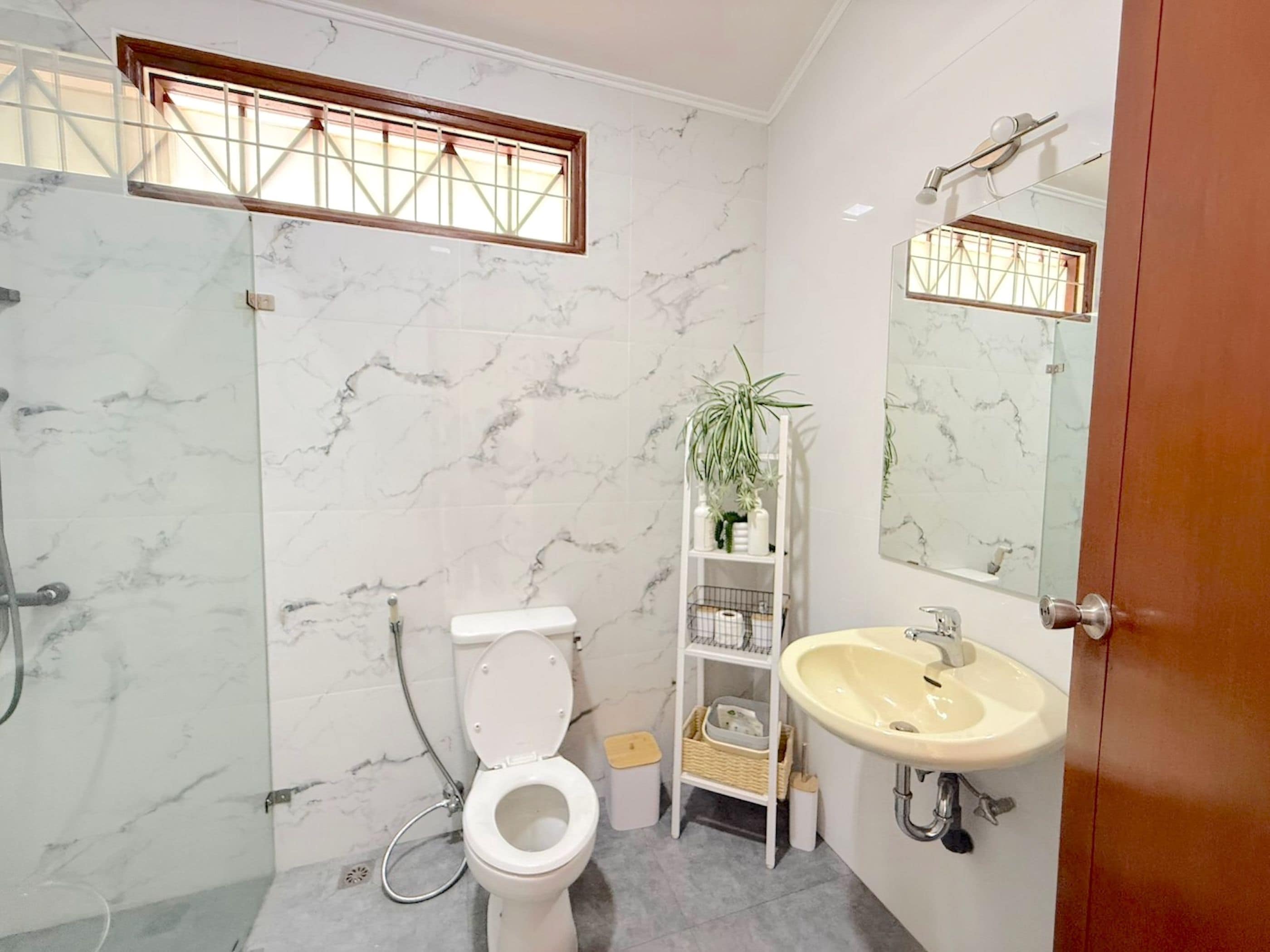 Un baño con inodoro, lavamanos, ducha y un estante con artículos de aseo.