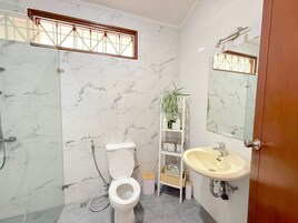 Un baño con inodoro, lavamanos, ducha y un estante con artículos de aseo.