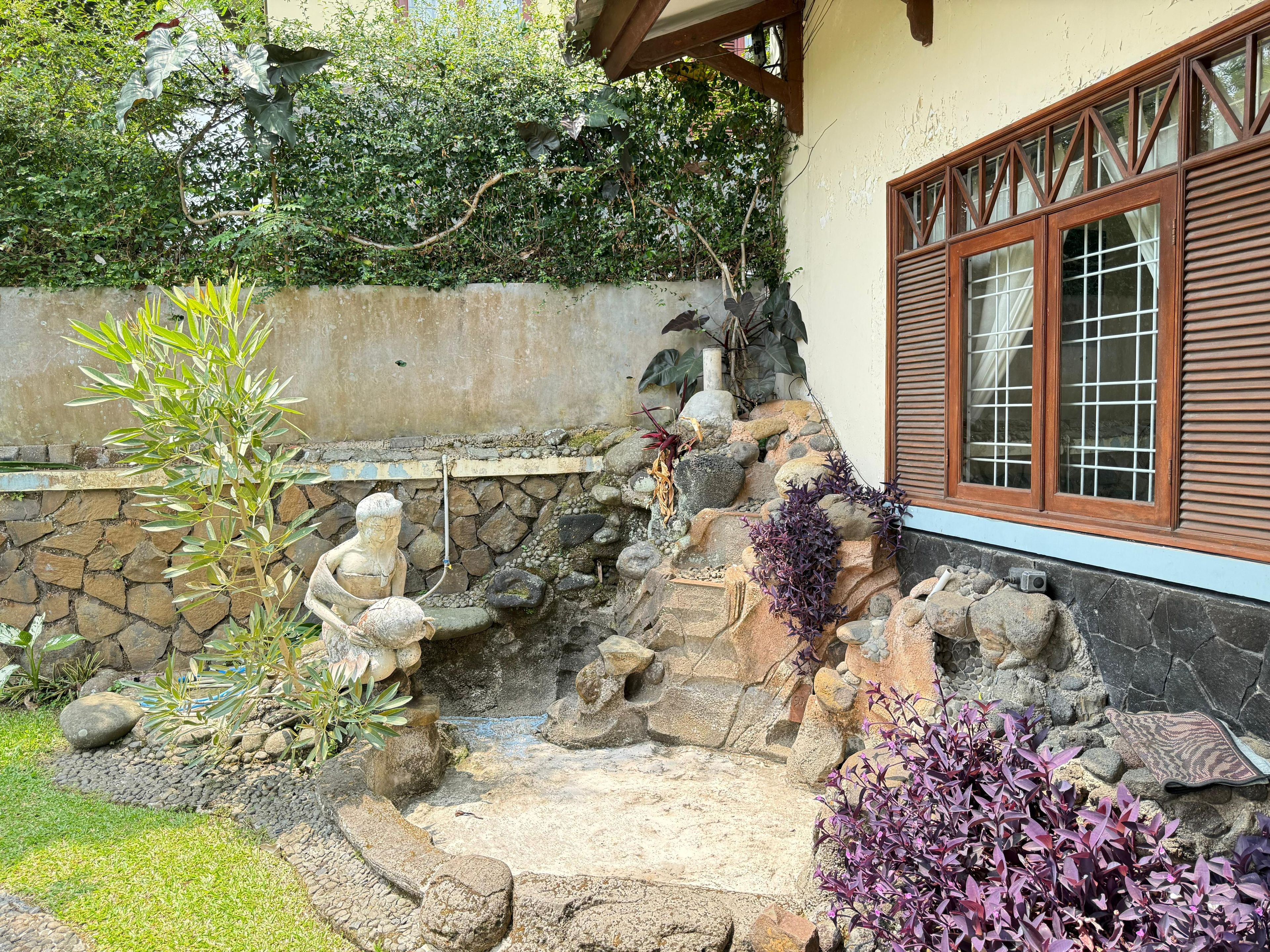 A garden with a stone wall, a statue, and various plants.
