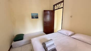 A room with two beds, a door, a painting on the wall, and a tiled floor.