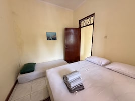 Una habitación con dos camas, una puerta, un cuadro en la pared y suelo de baldosas.