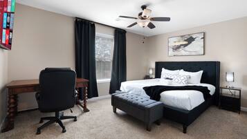 Een slaapkamer met een bed, bureau, stoel en een plafondventilator.