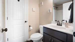 Ein Badezimmer mit Toilette und Waschbecken in Weiß, einem dunklen Wasserhahn über dem Waschbecken und einem Handtuch an der Wand.