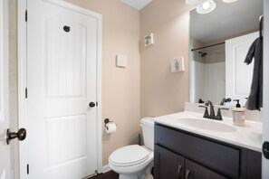 Ein Badezimmer mit Toilette und Waschbecken in Weiß, einem dunklen Wasserhahn über dem Waschbecken und einem Handtuch an der Wand.