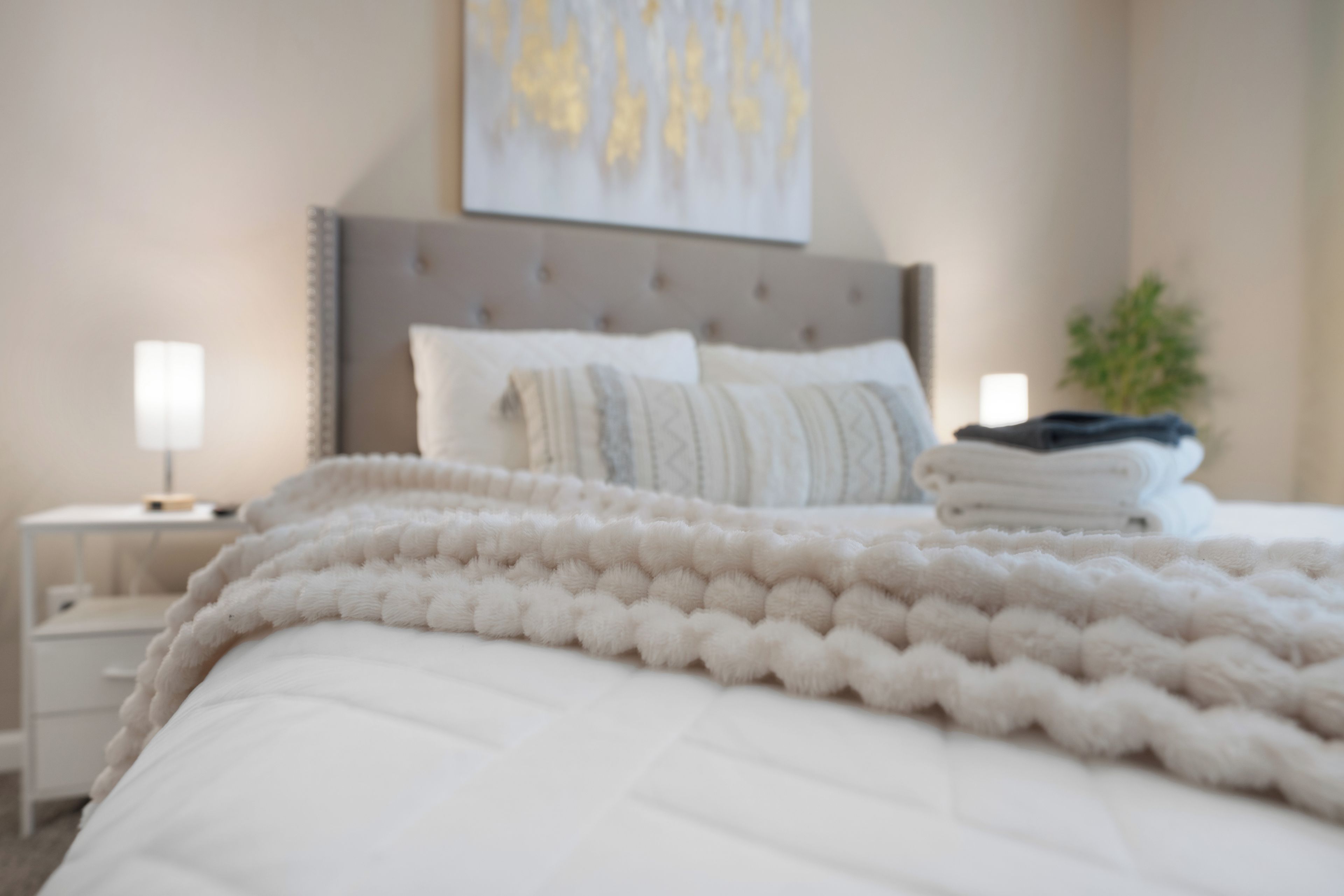 A neatly made bed with a fluffy white blanket, a bedside lamp, and a folded towel on the nightstand.