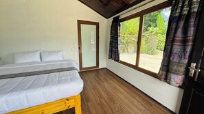 Un dormitori amb llit, terres de fusta, una finestra amb cortines i una porta.