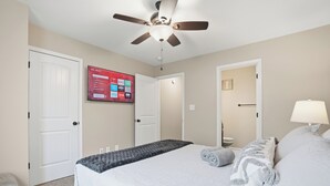 Een hotelkamer met een bed, een plafondventilator, een aan de muur bevestigde televisie en een deur.