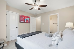 A hotel room with a bed, a ceiling fan, a TV mounted on the wall, and a door. - Smithson Getaway-Wi-Fi|King Bed | Desk | Private Bath in Each Room (Clarksville)