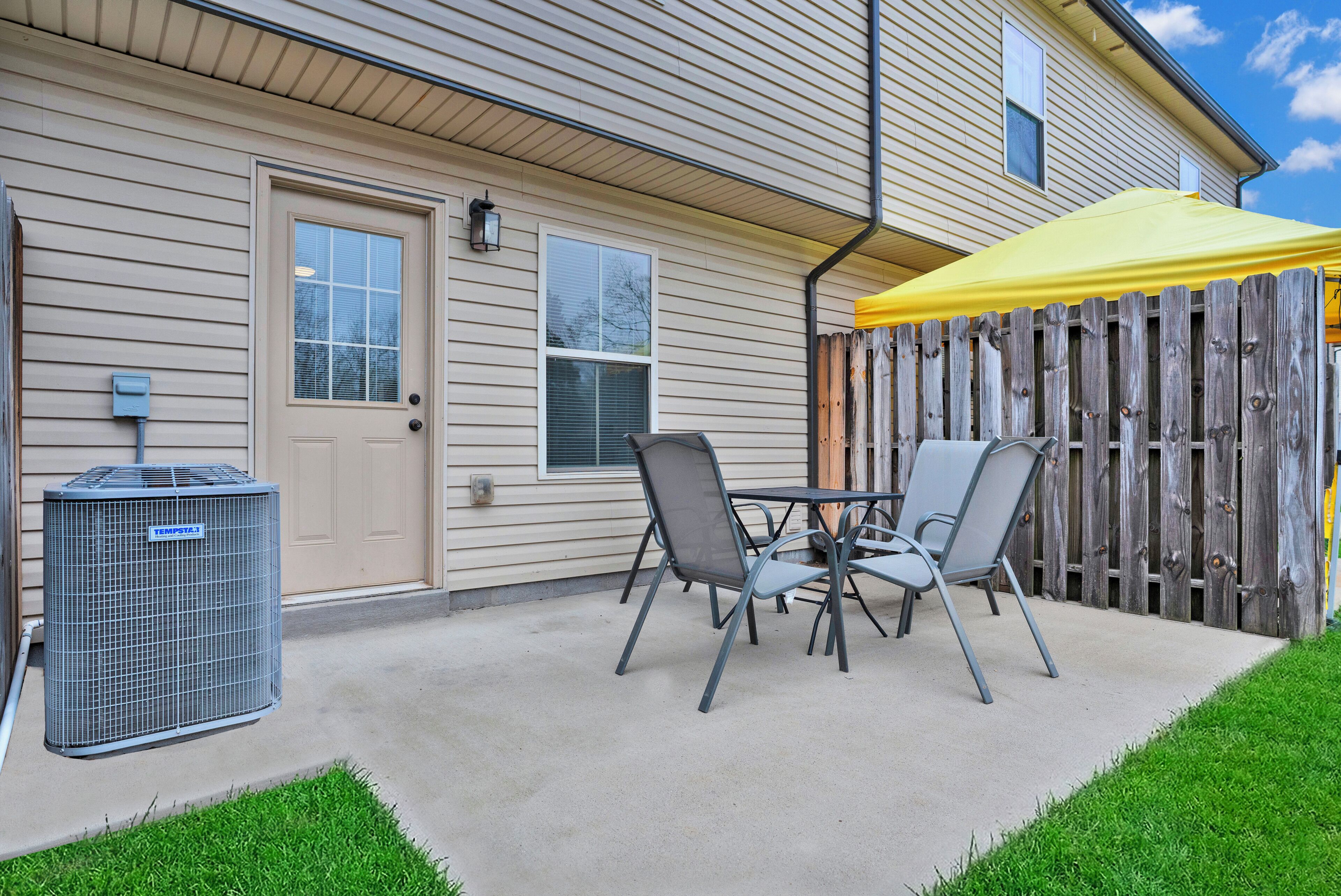 A patio with a table and chairs, a yellow umbrella, and a wooden fence.