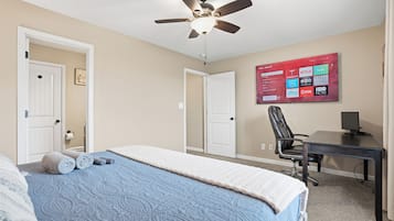 A bedroom with a bed, a ceiling fan, a desk, and a TV displaying streaming services.