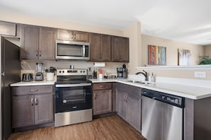 A modern kitchen with stainless steel appliances, wooden cabinets, and a dishwasher. - Smithson Getaway-Wi-Fi|King Bed | Desk | Private Bath in Each Room (Clarksville)