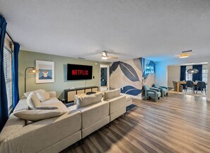 Ein modernes Wohnzimmer mit einem Ecksofa, einem Flachbildfernseher und einem Essbereich mit Stühlen und einem Tisch.