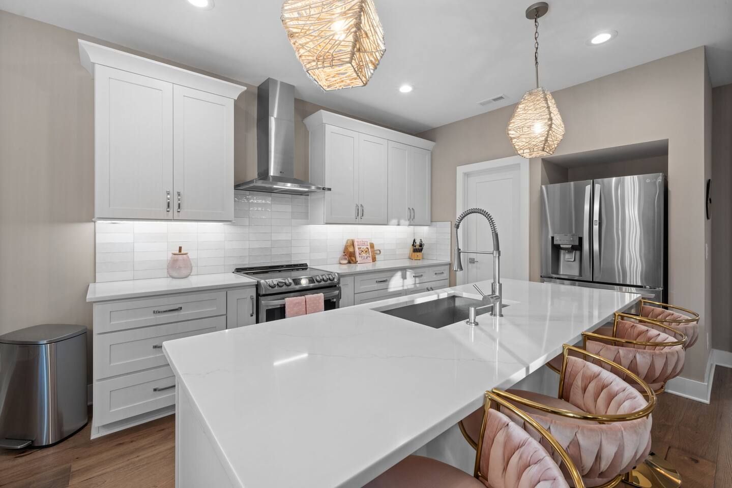 A modern kitchen with white cabinetry, a stainless steel range, a central island with a sink, and pendant lighting.