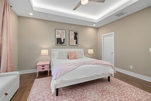 A bedroom with a bed, bedside tables, a ceiling fan, and two wall-mounted artworks. - Pink Dream House | Game Room | Separate Loft Suite | 2mi to Raleigh (Raleigh)