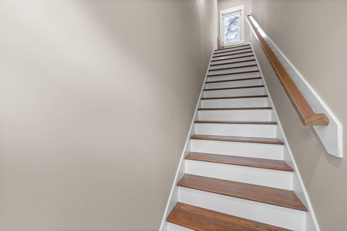 A staircase with wooden steps and white handrails, leading to a landing with a framed picture.