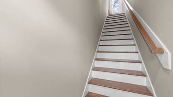 A staircase with wooden steps and white handrails, leading to a landing with a framed picture.