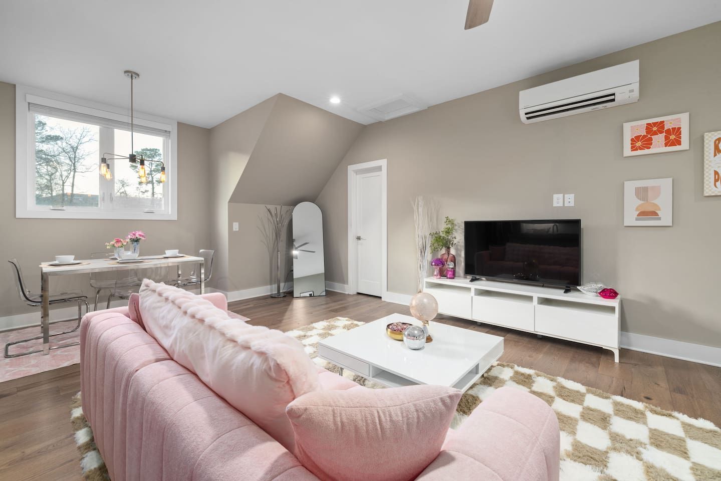 A modern living room with a pink sofa, a white coffee table, a flat-screen TV, and a dining area with a table and chairs.