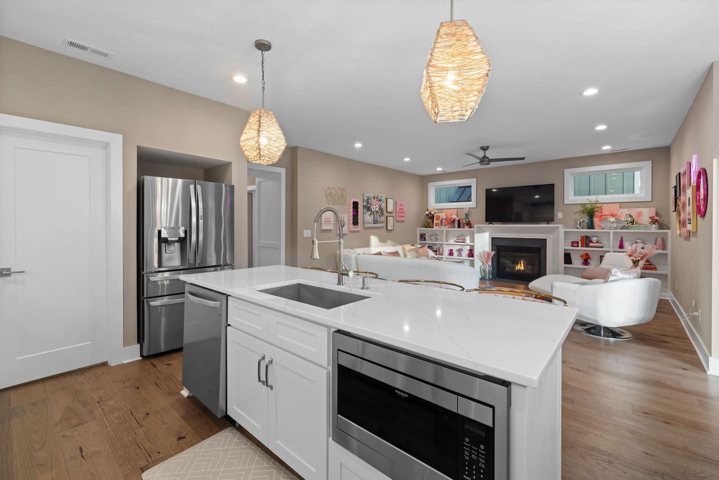 Una cocina moderna con armarios blancos, electrodomésticos de acero inoxidable, una isla central con pileta e iluminación colgante.