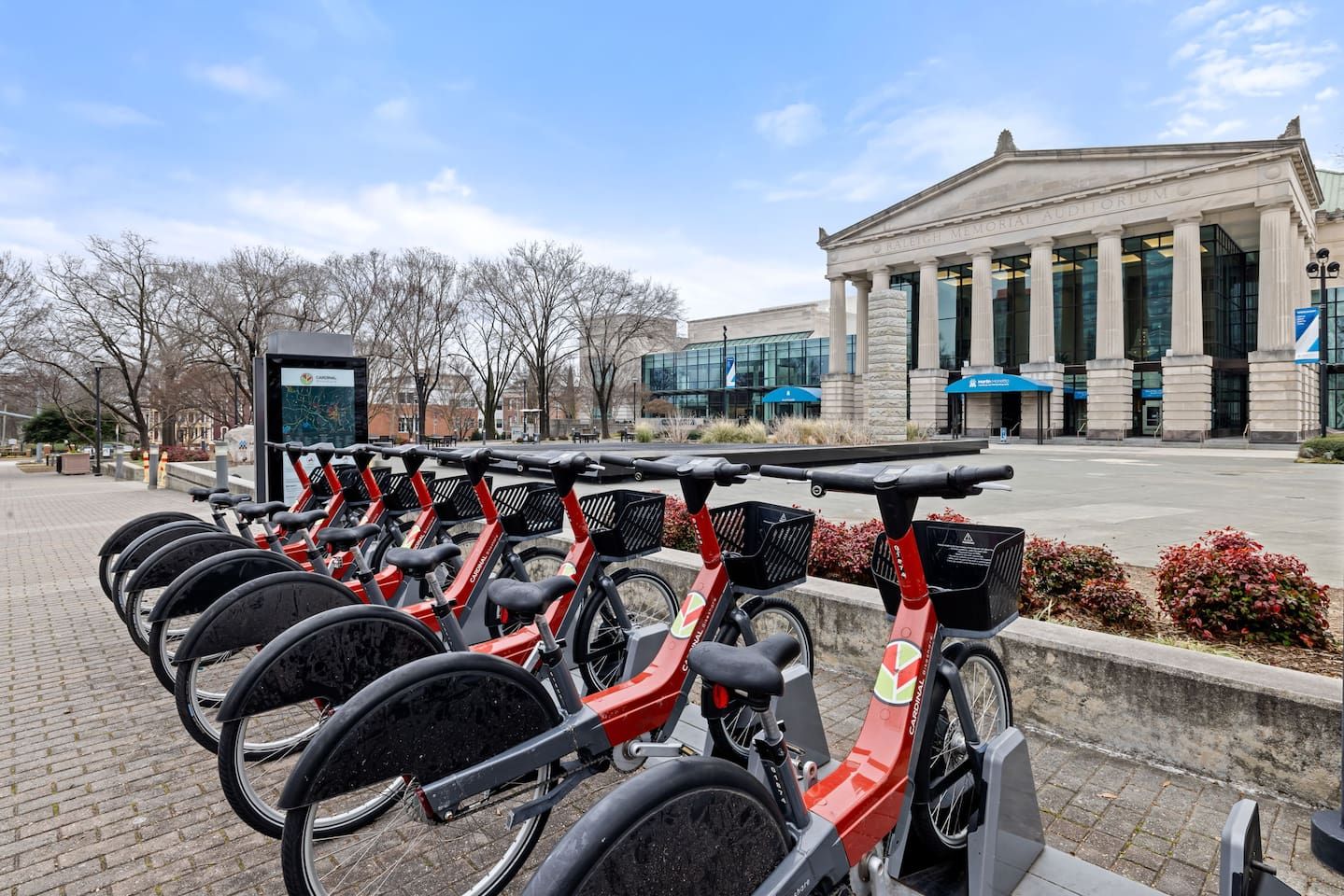 A row of red electric bikes parked in front of a building with columns and a glass facade.