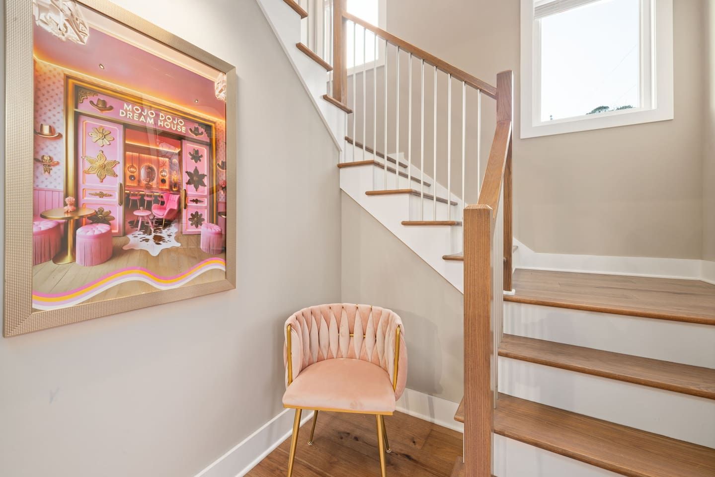 A staircase with wooden steps and white railings, a pink chair, and a framed picture of a dream house.