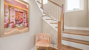 A staircase with wooden steps and white railings, a pink chair, and a framed picture of a dream house.
