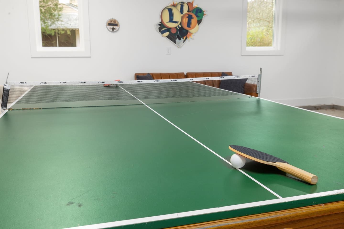 A green indoor table tennis table with a net, a paddle, and a ball.