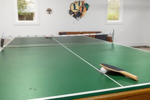 A green indoor table tennis table with a net, a paddle, and a ball. - Pink Dream House | Game Room | Separate Loft Suite | 2mi to Raleigh (Raleigh)