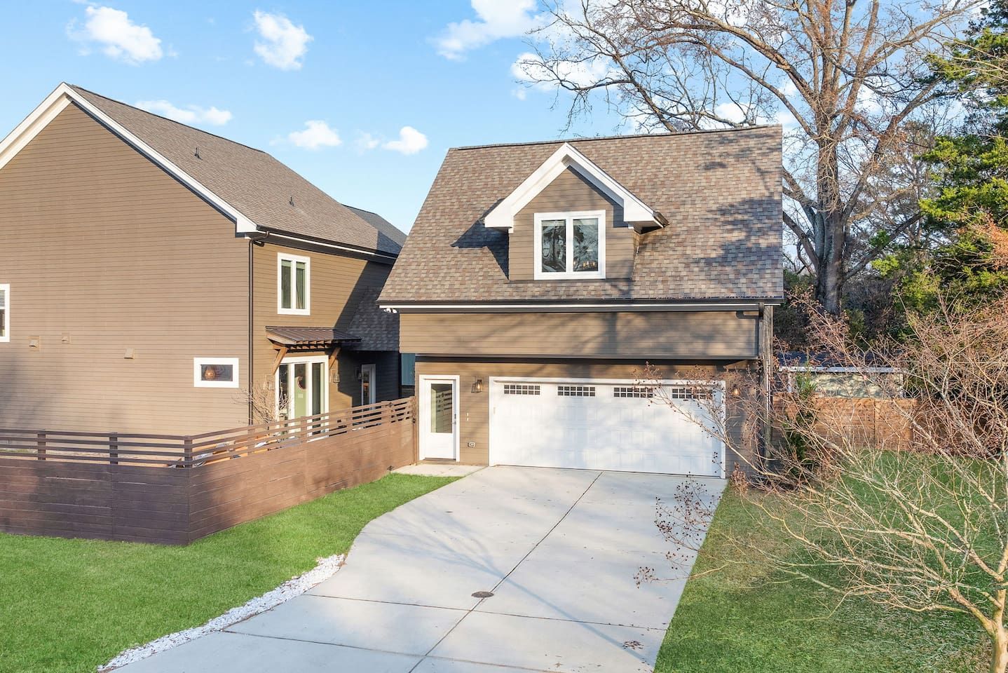 A two-story residential house with a visible garage door, a driveway, and a well-maintained lawn.