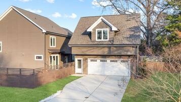 A two-story residential house with a visible garage door, a driveway, and a well-maintained lawn.