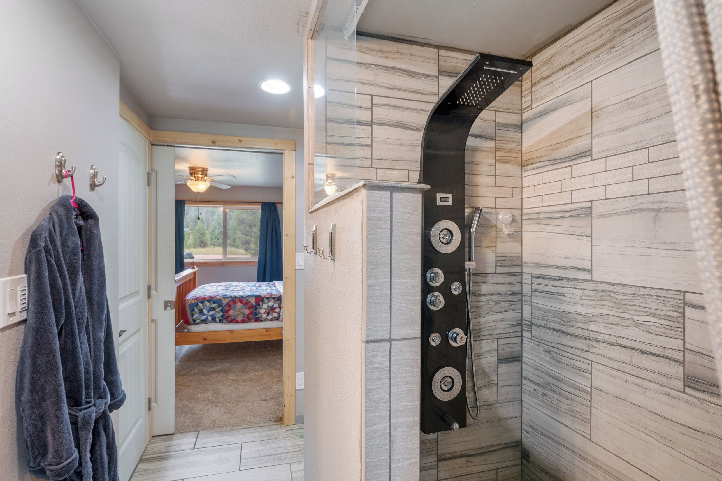 Een badkamer met een douche, een handdoekrek met handdoeken, en een bed zichtbaar door een geopende deur.