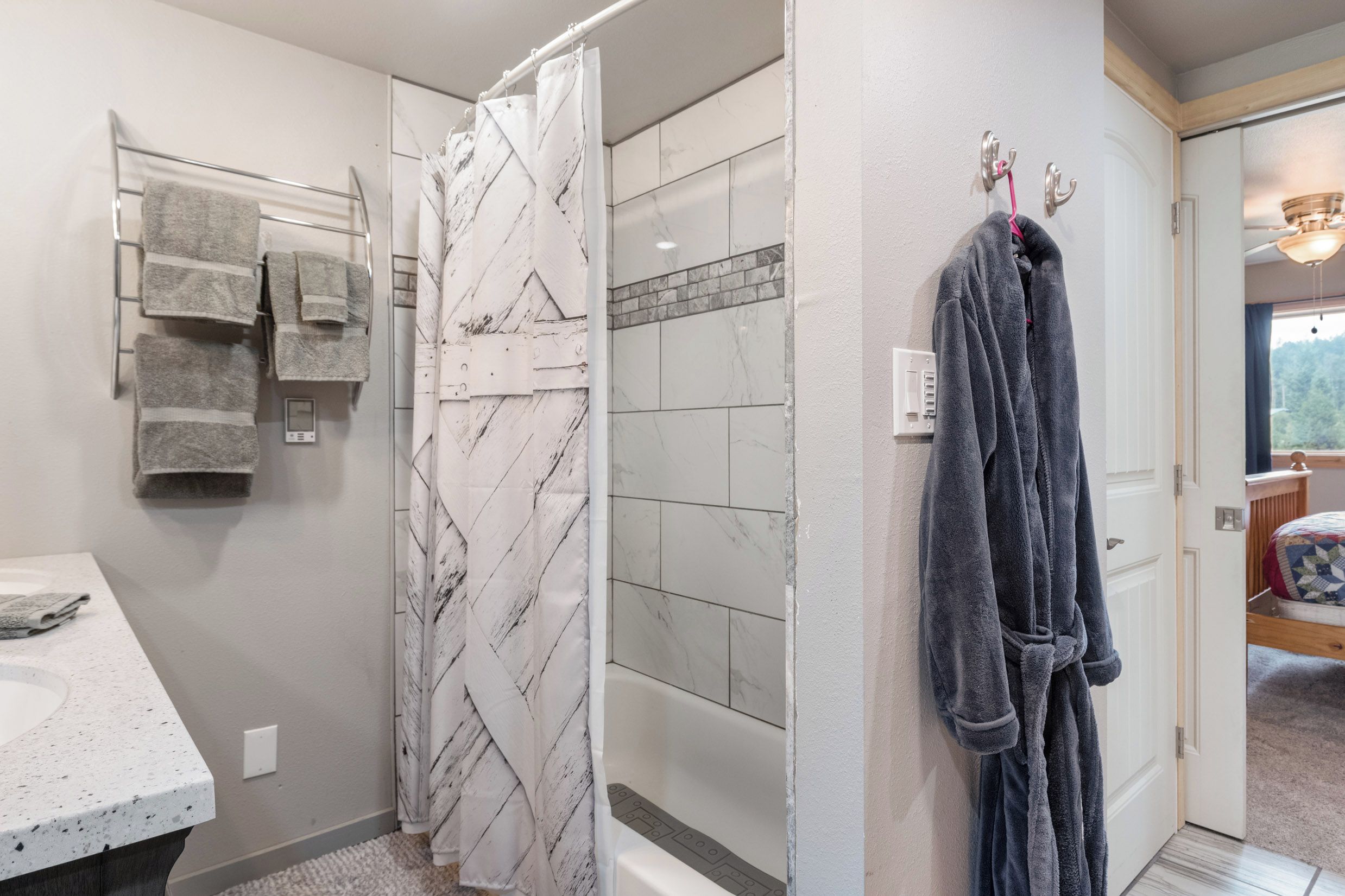 A bathroom with a shower, a towel rack, and a robe hanging on a hook.