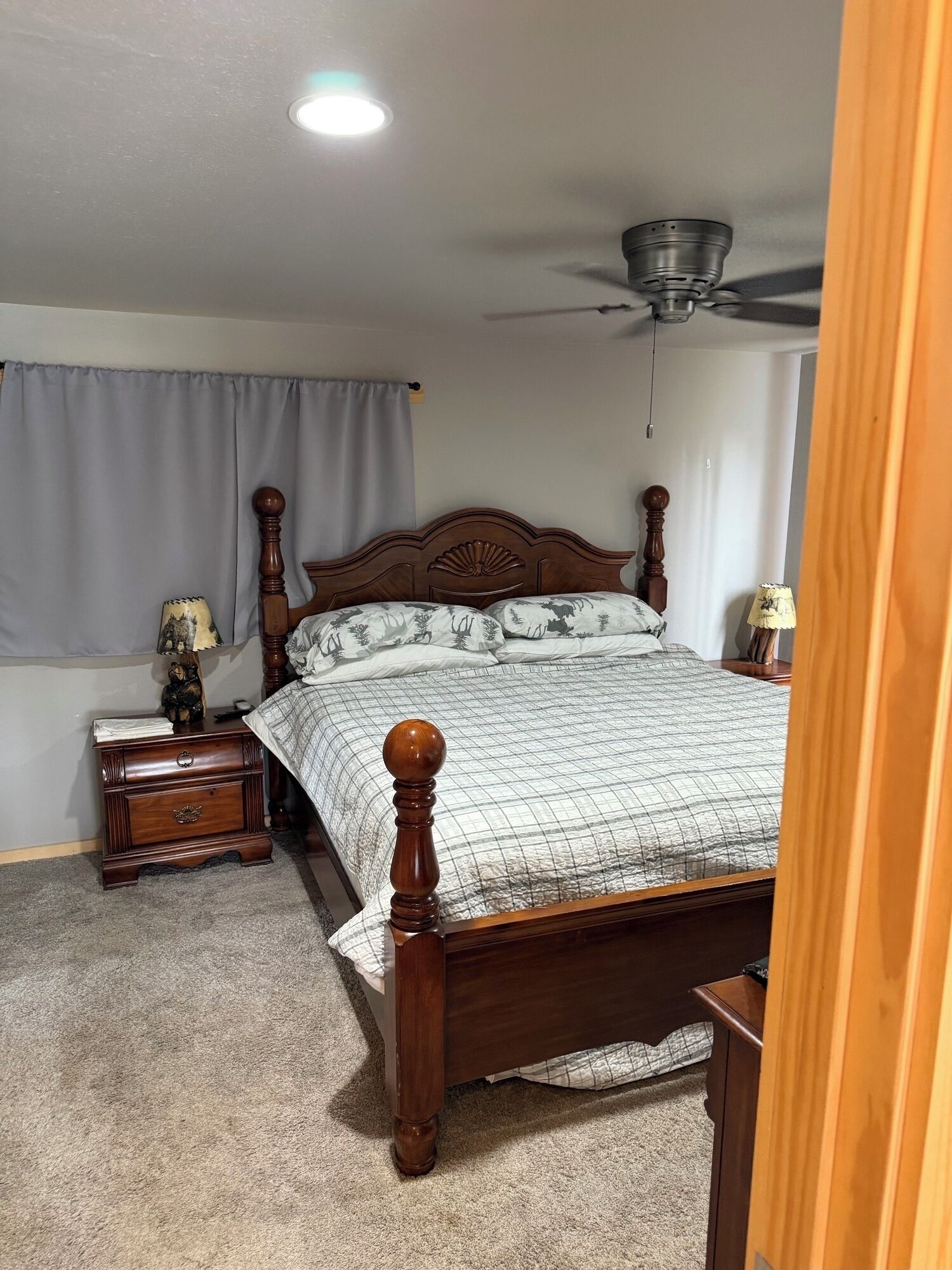 A bedroom with a wooden bed, a ceiling fan, and a nightstand with a lamp.