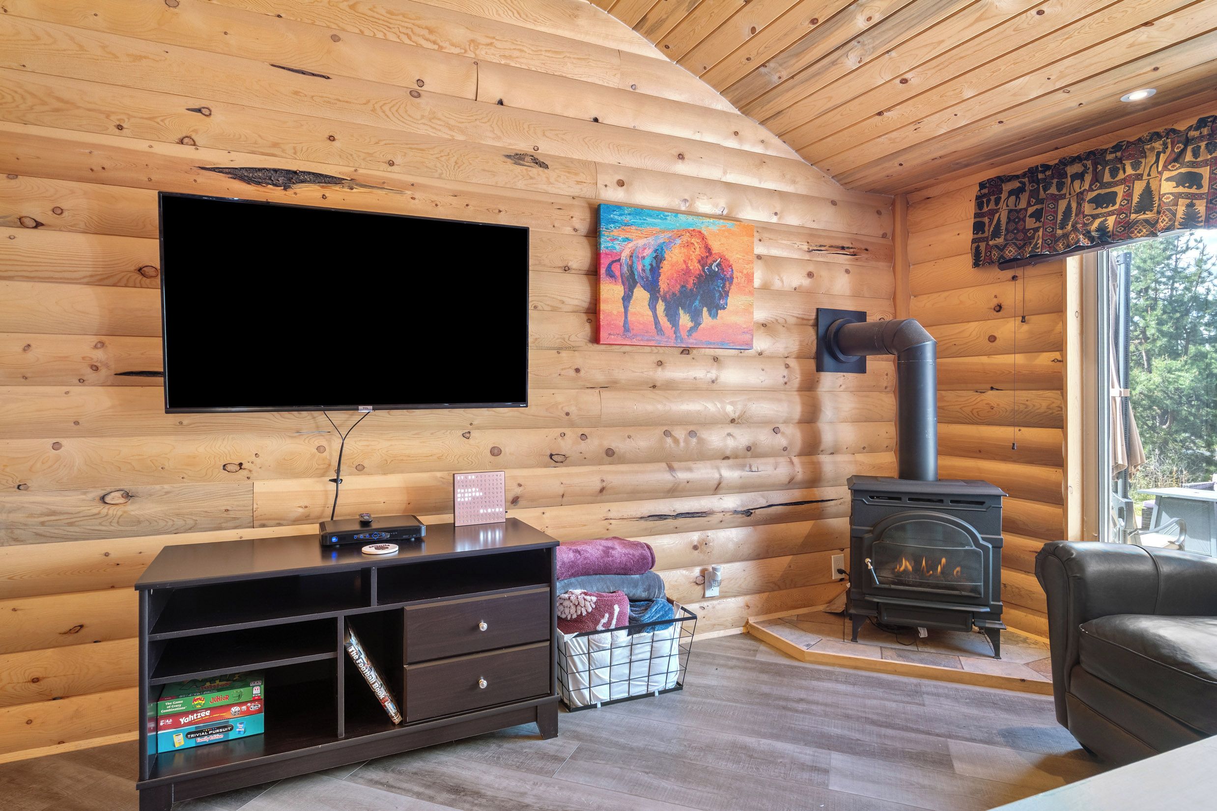 L’intérieur d’une cabane en rondins est aménagé avec un téléviseur à écran plat, une cheminée, un canapé et une console de jeux.