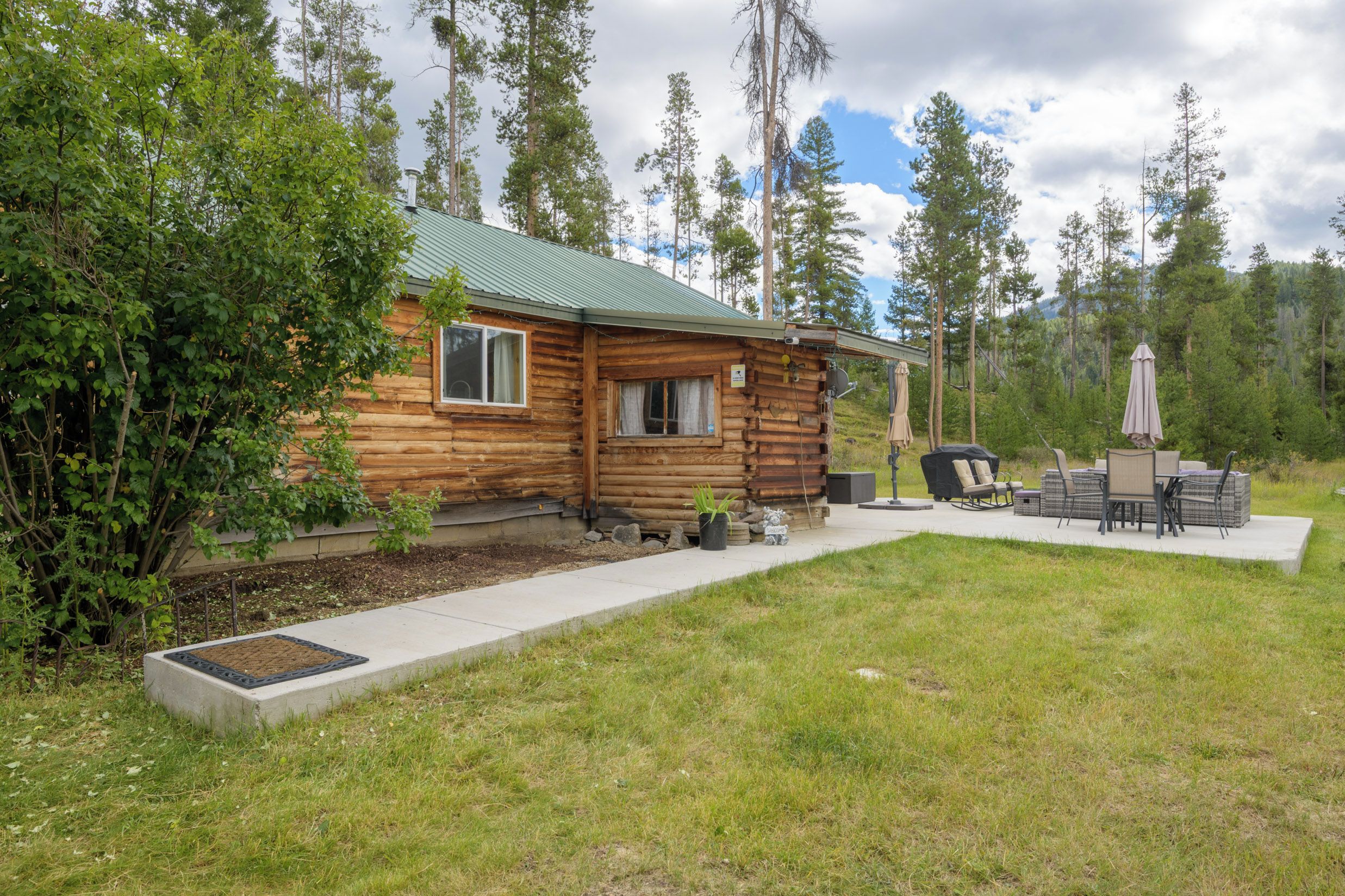 A log cabin with a green roof, surrounded by a grassy yard and tall trees.