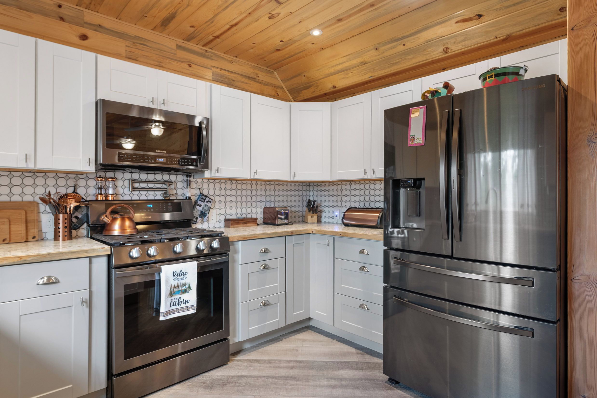 A modern kitchen with stainless steel appliances, white cabinets, and a wooden ceiling.