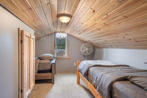 A small, cozy room with a sloped ceiling, a bed, a desk with a chair, and a window.