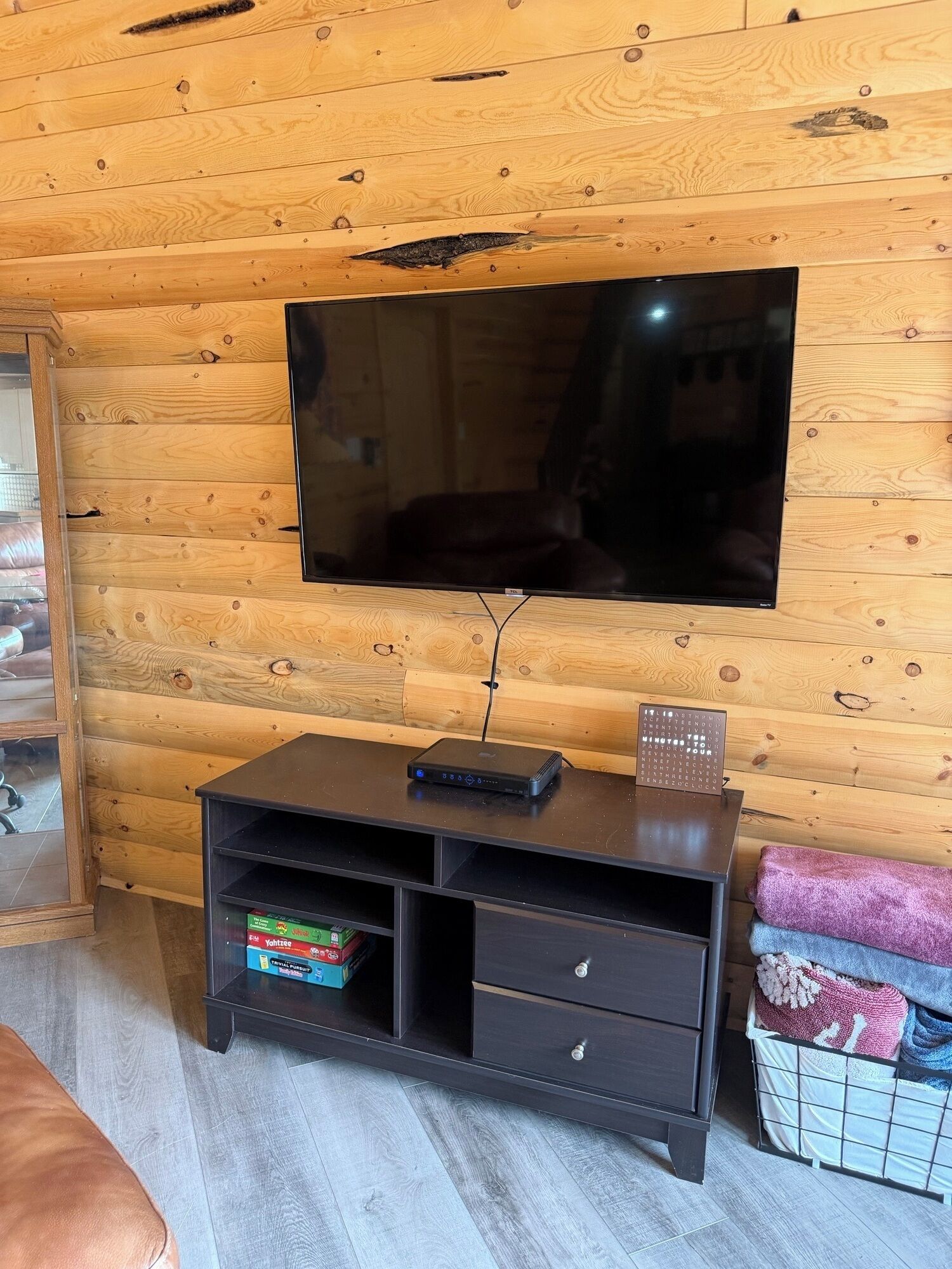Un intérieur en bois, avec un téléviseur à écran plat fixé au mur, un meuble en bois foncé doté de tiroirs et une petite table avec une télécommande.