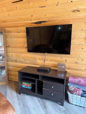 Ein Holzinterieur mit einem an der Wand montierten Flachbildfernseher, einem dunklen Holzschrank mit Schubladen und einem kleinen Tisch mit einer Fernbedienung.