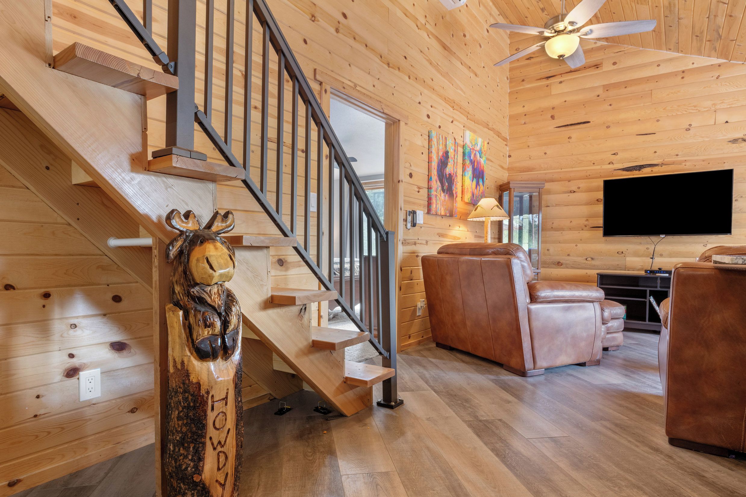 Un intérieur en bois avec un escalier, une sculpture murale, un canapé en cuir et un téléviseur à écran plat.
