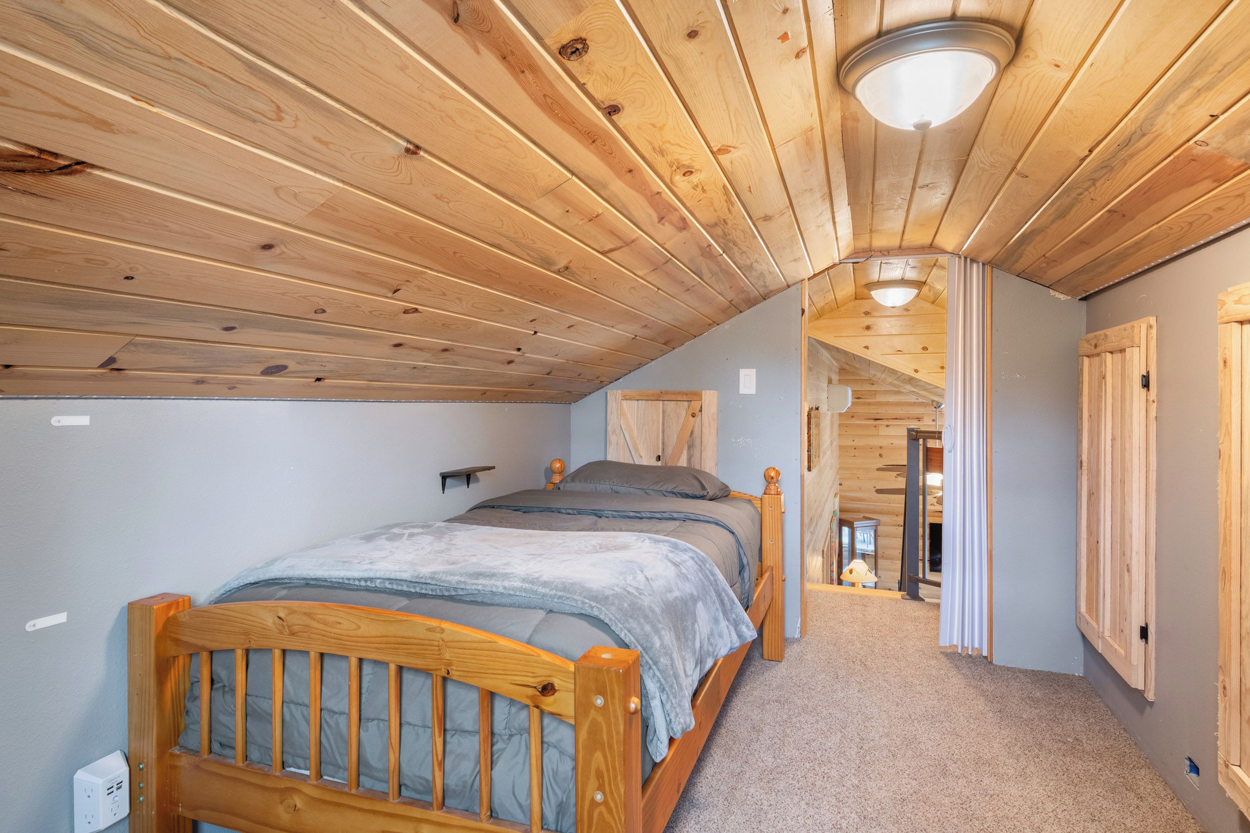 A bedroom with a wooden ceiling, a bed with a headboard, a bedside table, and a nightstand.