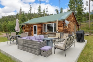 A log cabin with a patio area featuring outdoor furniture and a grill.
