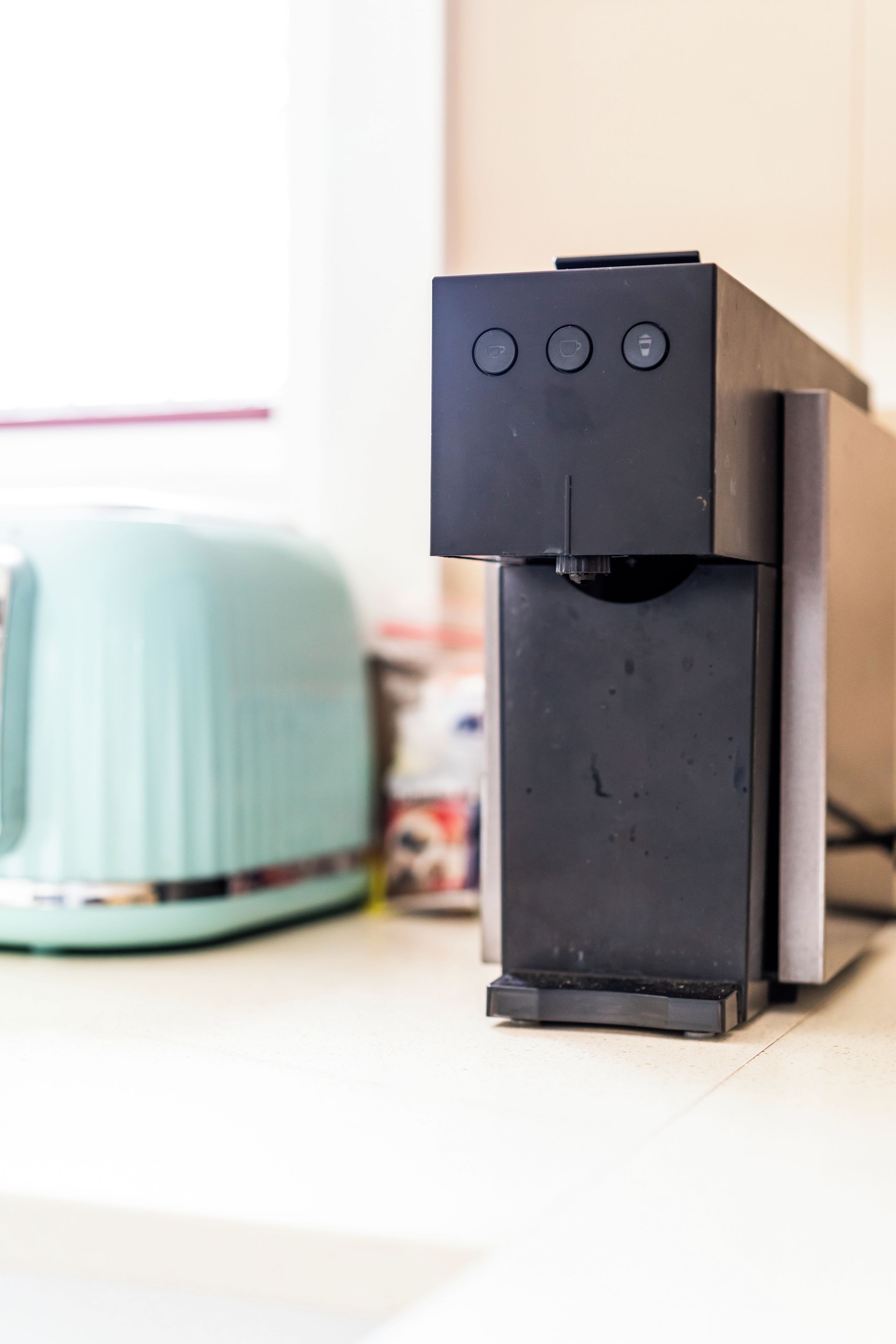 A coffee machine with buttons on the front, a toaster, and a container of sugar on a countertop.