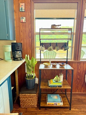 A cozy kitchen with wooden cabinets, a coffee maker, a potted plant, a wicker basket, and a window with a view of greenery.