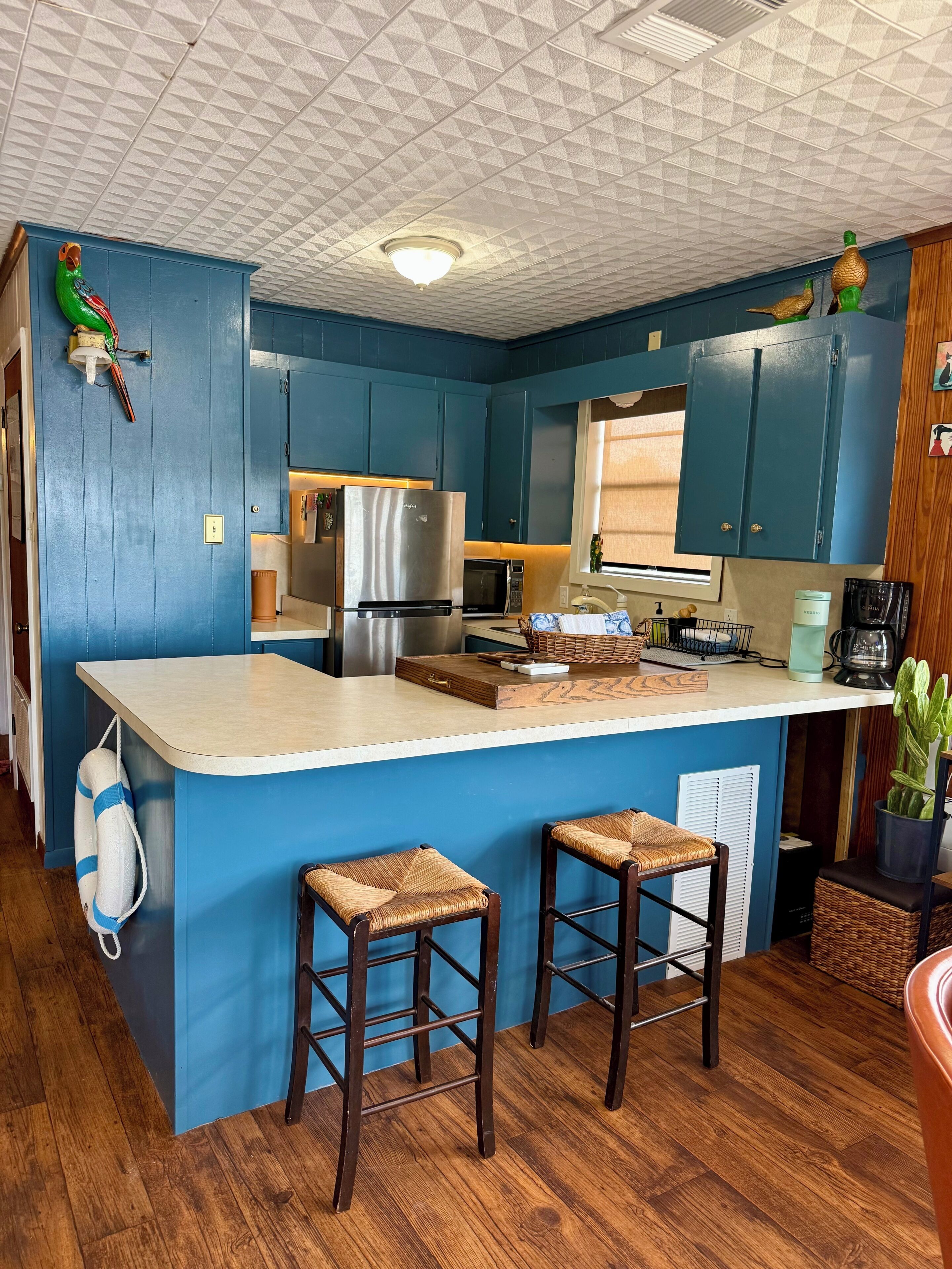 A kitchen with blue cabinets, a stainless steel refrigerator, a microwave, and a wooden island with two stools.
