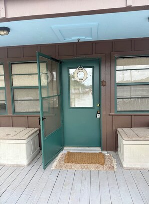 A teal door with a welcome mat, a window with a view, and a bench outside.