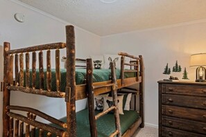 Ein Stockbett mit rustikalem Holzbau, eine Kommode mit Schubladen und eine Lampe auf einem Nachttisch.