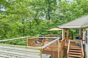 Eine Holzterrasse mit Gartenmöbeln und einer überdachten Sitzgelegenheit, umgeben von dichtem Wald.