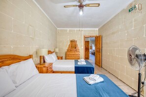 Ein Hotelzimmer mit zwei Betten, einem Holzschrank, einem Deckenventilator und einem Wandventilator.