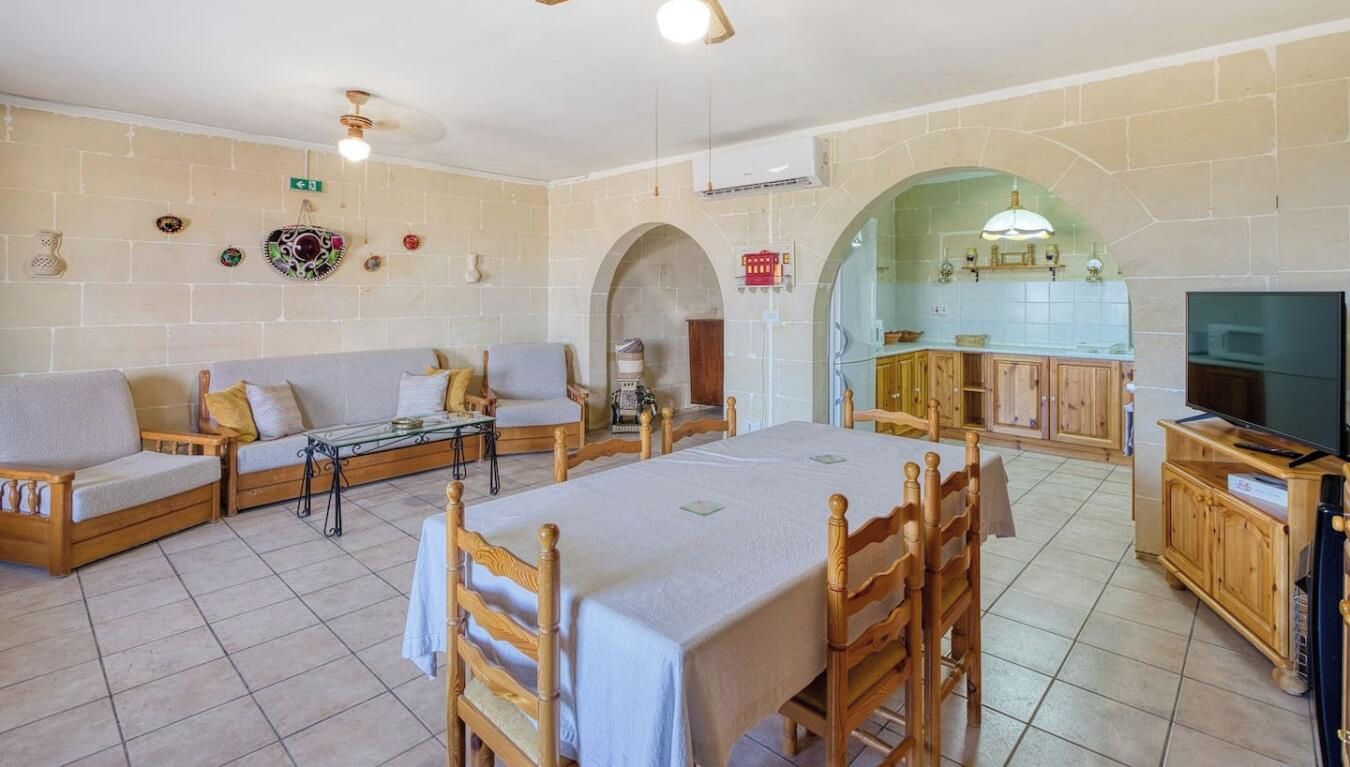 A living room with a sofa set, a dining table with chairs, a kitchen area with cabinets, and a television.