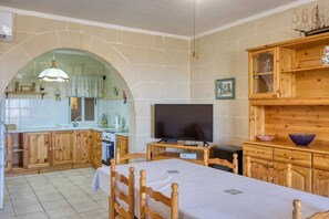 A compact room with a dining table, a television, and wooden cabinets. - Stone Apt in Nadur | Terrace & Patio | Sleeps 6 (Nadur)